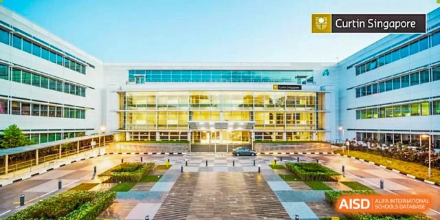A modern school building with a bright yellow and glass exterior dominates the view, looking across a wide, paved entrance courtyard at Cambridge International School Litai College. SISU.