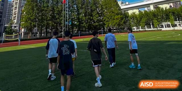 Students in athletic wear walk across a grassy field during an outdoor activity at Cambridge International School Litai College. SISU.