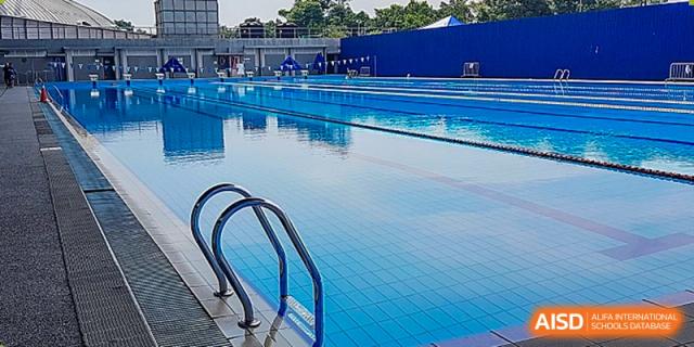 A clear, bright blue outdoor swimming pool with stainless steel steps and lane lines visible at Cambridge International School Litai College. SISU.