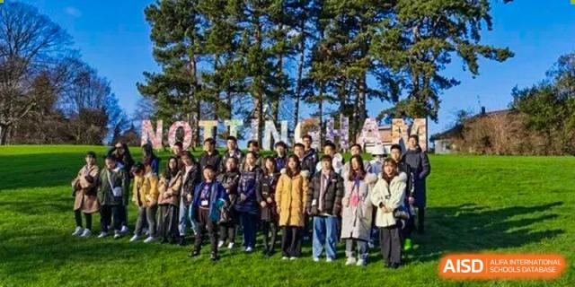 A large group of students and teachers pose together for a photograph outdoors surrounded by trees at Cambridge International School Litai College. SISU.