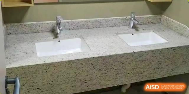 A speckled granite bathroom countertop with two white sinks and metal faucets visible at Cambridge International School Litai College. SISU.