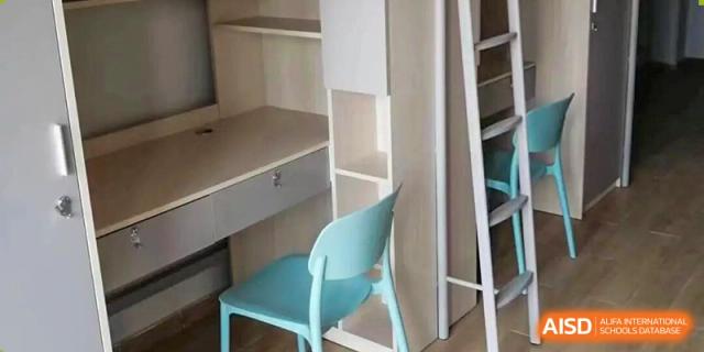 A close-up of a student dormitory room's desk, shelving unit, and a light blue study chair at Cambridge International School Litai College. SISU.
