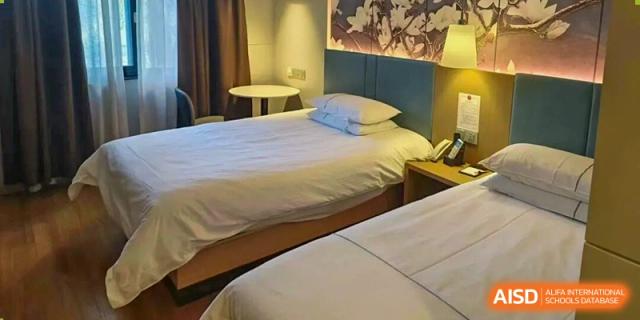 A dormitory room featuring two twin beds with white bedding, nightstands, and soft lighting at Cambridge International School Litai College. SISU.