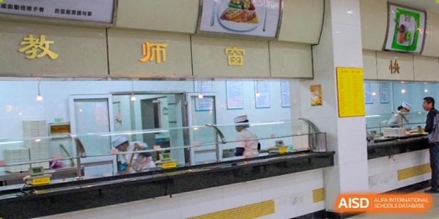 A food service counter area in the canteen where staff wearing hats are preparing and serving food at Cambridge International School Litai College. SISU.