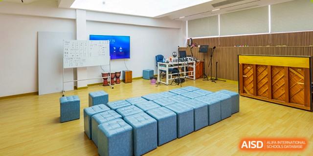 A modern music or activity room featuring rows of blue padded stools, a keyboard station, and drums at the Shenzhen Academy of International Education.