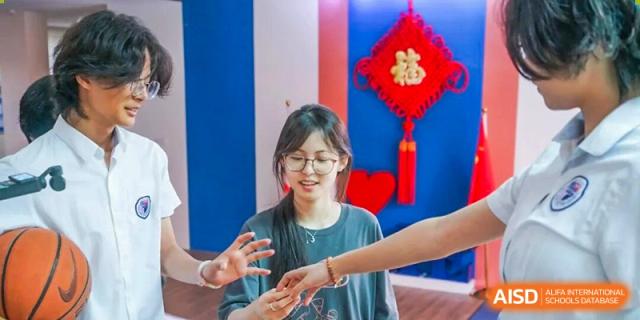 A smiling student engages in a hands-on activity with classmates in front of a colorful wall display at the Shenzhen Academy of International Education.