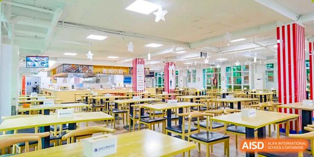 A large, clean, and empty school cafeteria with rows of yellow tables and black chairs at the Shenzhen Academy of International Education.