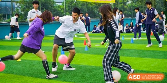Students engage in a lively team-building activity kicking a pink ball on a green turf field at Shenzhen Academy of International Education.