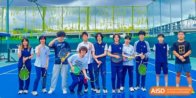 A group of students in athletic wear pose with tennis rackets on a blue outdoor sports court at Shenzhen Academy of International Education.