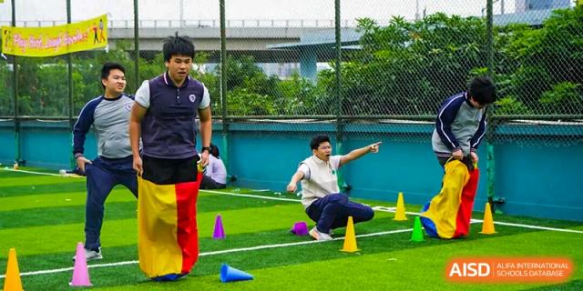 Students participate in a competitive sack race on the green turf field during an outdoor sports day event at Shenzhen Academy of International Education.