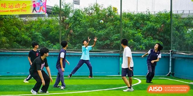 A group of students play a lively game of volleyball or catch on the school's outdoor green turf sports field at Shenzhen Academy of International Education.