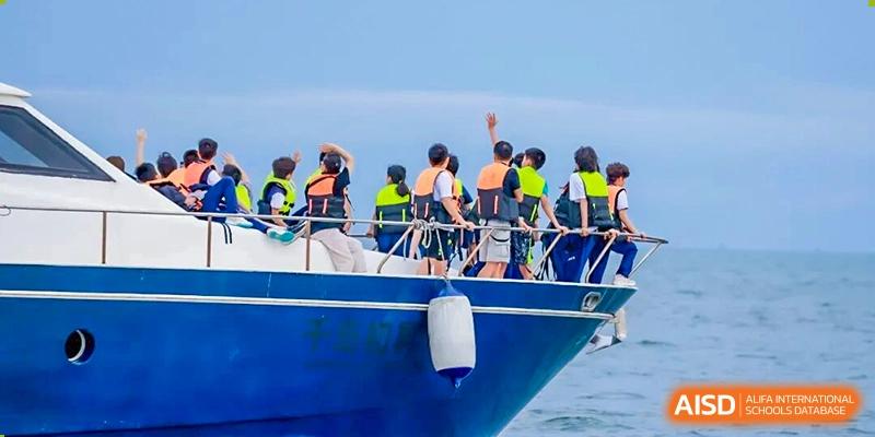 A large group of students wearing life vests gather on the deck of a blue boat during an outdoor water excursion at Shenzhen Academy of International Education.