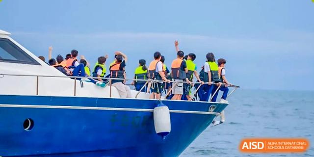 A large group of students wearing life vests gather on the deck of a blue boat during an outdoor water excursion at Shenzhen Academy of International Education.