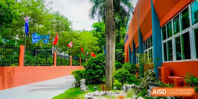Lush green campus featuring colorful flags and a modern orange building exterior under a clear sky at Shenzhen Academy of International Education.