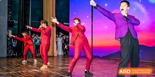 A talented student dressed in a striking red suit performs a dynamic dance routine on a stage with a colorful backdrop at Shenzhen Academy of International Education.