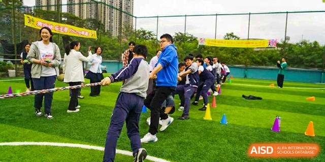Students participating in a high-energy game of tug-of-war on a green outdoor sports field during a school event at Shenzhen Academy of International Education.
