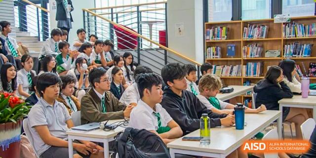 A group of secondary students sitting together on a staircase during a presentation or school gathering at Shen Wai International School.