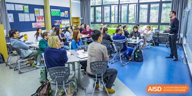 A group of educators and parents attend a workshop or presentation in a modern classroom setting at Shen Wai International School.