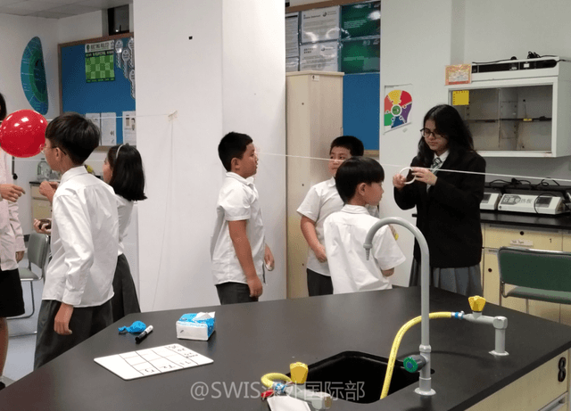 Young students standing by a lab station engage in a hands-on science demonstration with their teacher at Shen Wai International School.