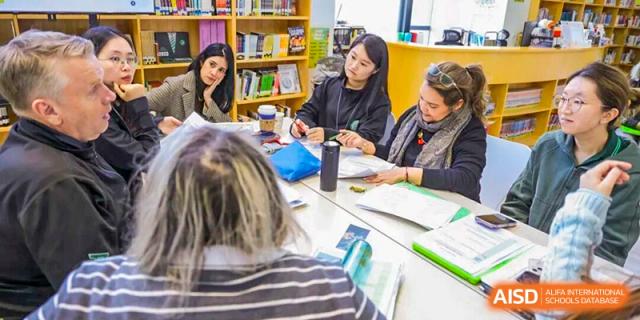 Teachers or staff members sit around a table engaged in a collaborative planning meeting or training at Shen Wai International School.