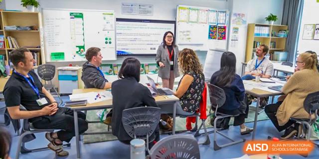 A teacher leads a professional development workshop for staff in a modern classroom setting with a digital whiteboard at Shen Wai International School.