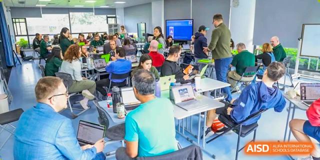 A large group of adults work on laptops during a technology-focused training session in a spacious room at Shen Wai International School.