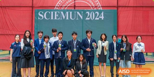 A group of students in formal school uniforms pose together in front of a green backdrop for the 2024 SWIEMUN conference at Shen Wai International School.