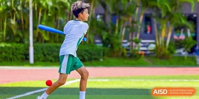 A young male student athlete in a green and white sports uniform runs across a lush green field during an outdoor physical education class at Shen Wai International School.