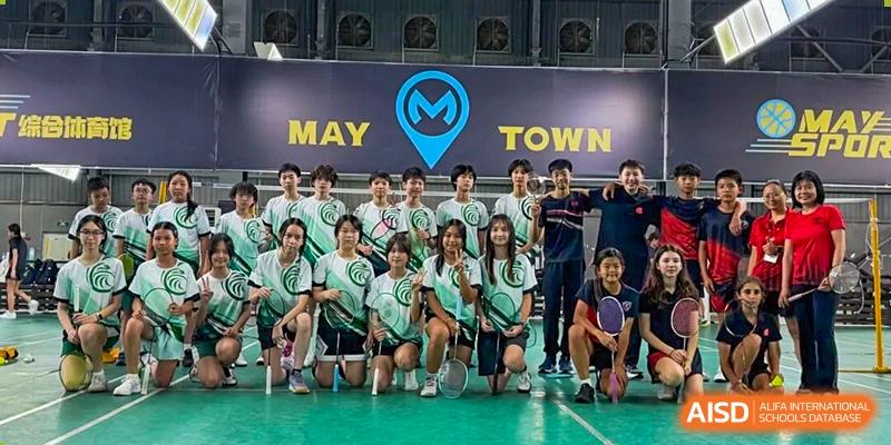 The student badminton team poses for a group photo in their uniforms on an indoor court under a "May Town" sign at Shen Wai International School.