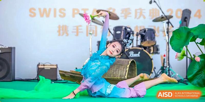A student performer in an elegant blue and purple traditional costume performs a graceful dance pose on a stage during a school event at Shen Wai International School.