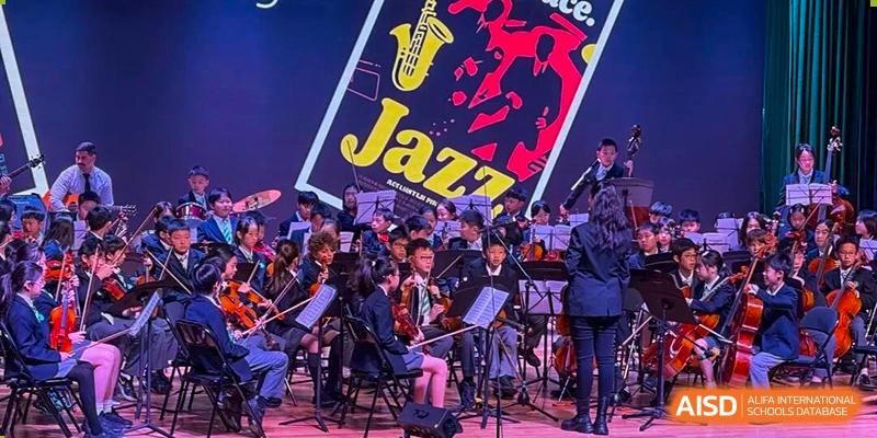 A student jazz orchestra performs with violins and other instruments in front of a colorful "Jazz" backdrop at Shen Wai International School.