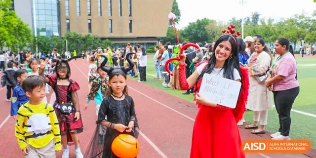 A young girl in a black costume and horns holds a pumpkin bucket during an outdoor parade at Shen Wai International School.