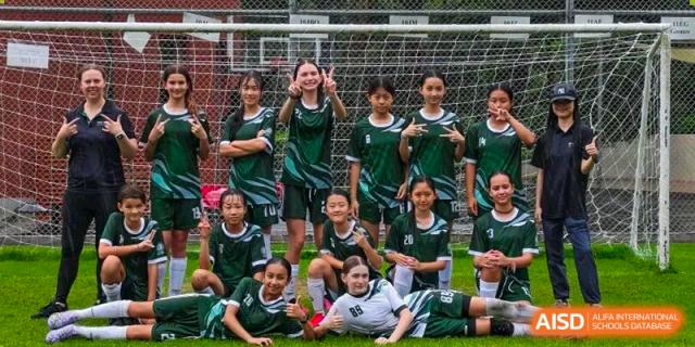 A girls' football team in green and white uniforms poses together on a grassy field at Shen Wai International School.