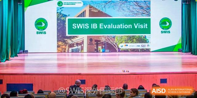 A large digital screen on a stage displays "SWIS IB Evaluation" to an audience in a theater at Shen Wai International School.