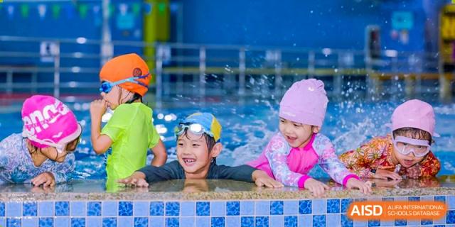 Two young children wearing colorful swim caps and goggles smile and play in the water at Shen Wai International School.