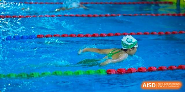 A student swimmer in a green swimsuit and white cap performs a stroke during a race in the pool at Shen Wai International School.
