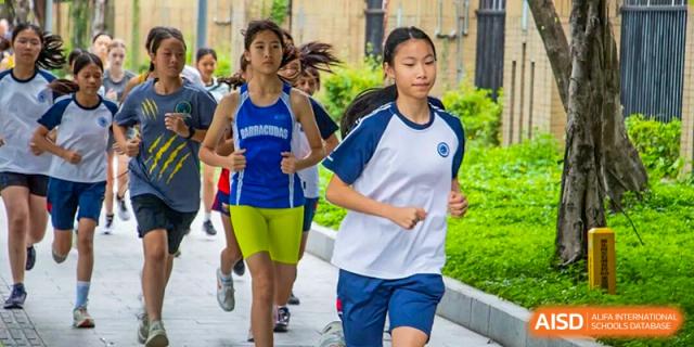 Two female students in athletic gear focus on their form while running together on an outdoor path at Shen Wai International School.