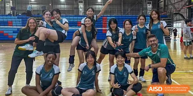 A cheerful group of student athletes in sports uniforms posing together on an indoor volleyball court at Shen Wai International School.