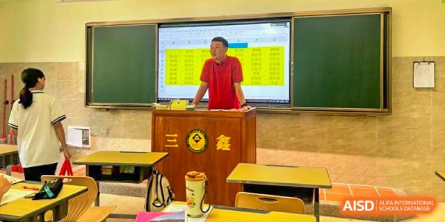 An instructor in a red polo shirt stands at a wooden podium in front of a digital spreadsheet during a lecture at Zhongshan Sanxin School International Department.