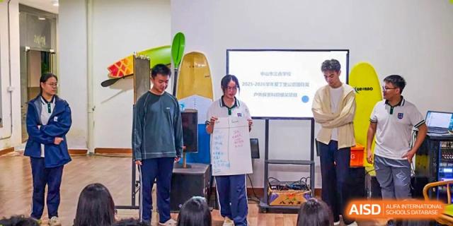 A student stands at the front of the room holding a large poster while presenting a project to her peers at Zhongshan Sanxin School International Department.