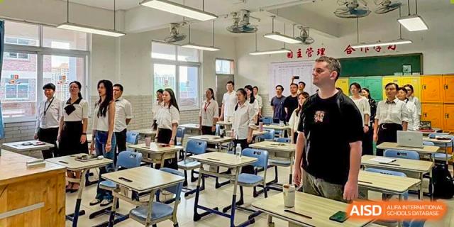 A diverse group of students and a teacher stand together in a bright, modern classroom during a group activity at Zhongshan Sanxin School International Department.