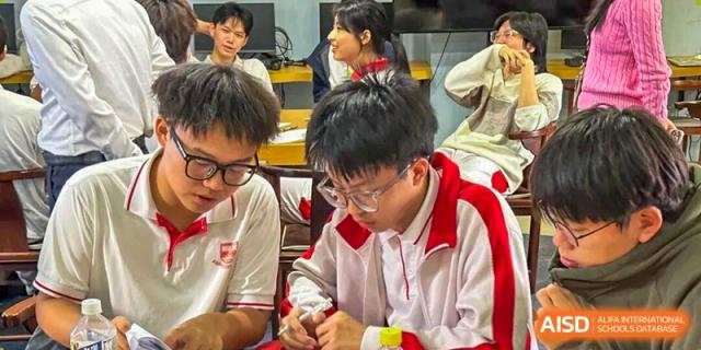 Students in red and white jackets work closely together at a lab table, focusing on a shared assignment at Zhongshan Sanxin School International Department.