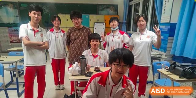A group of students in red and white uniforms pose for a photo in a classroom with colorful lockers in the background at Zhongshan Sanxin School International Department.