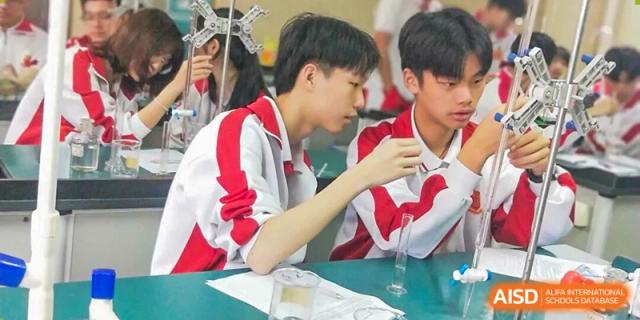 Two students collaborate on a science experiment, carefully measuring liquids into a graduated cylinder at Zhongshan Sanxin School International Department.