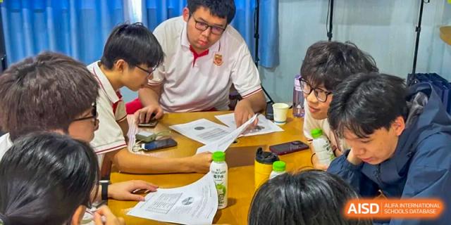 Several students sit around a table focusing on paperwork and digital devices during a collaborative study session at Zhongshan Sanxin School International Department.