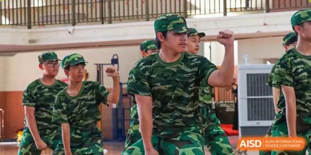A young man in a green camouflage uniform stands in a focused, athletic pose during a training exercise or performance at Zhongshan Sanxin School International Department.