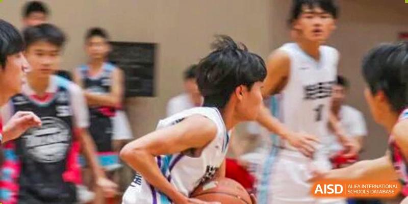 A close-up, action-oriented shot of a male student in a white jersey dribbling a basketball during a competitive game at Zhongshan Sanxin School International Department.