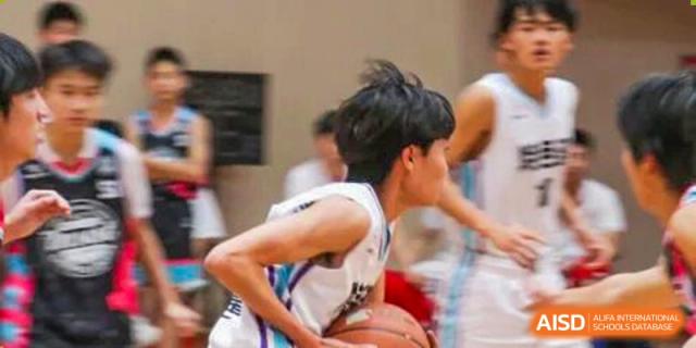 A close-up, action-oriented shot of a male student in a white jersey dribbling a basketball during a competitive game at Zhongshan Sanxin School International Department.