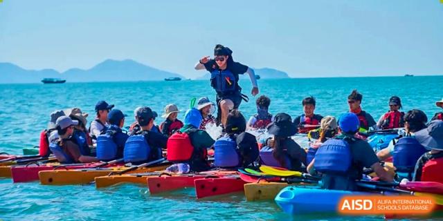 Students wearing life jackets sit in a row of colorful kayaks on the blue ocean water during a school trip with Zhongshan Sanxin School International Department.