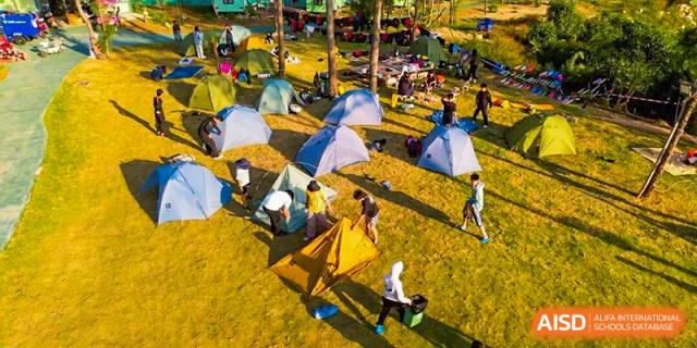 An aerial view of many colorful tents set up on a grassy field during an overnight school camping trip organized by Zhongshan Sanxin School International Department.